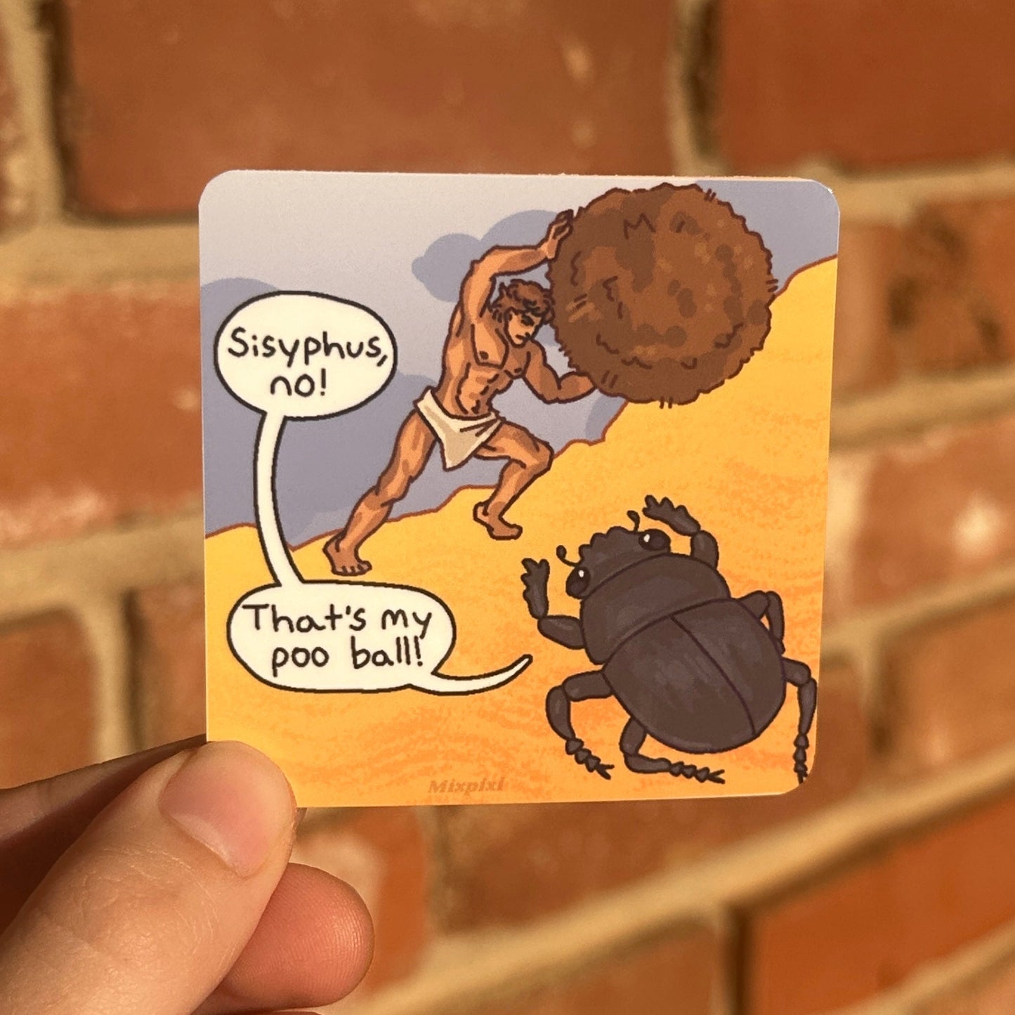 A hand holds a square printed card featuring a cartoon illustration of a figure carrying a large brown mound while a black beetle looks on, with speech bubbles reading 'Sisyphus no!' and 'That's my poo ball!'. The background is a blurred red-brown brick wall.