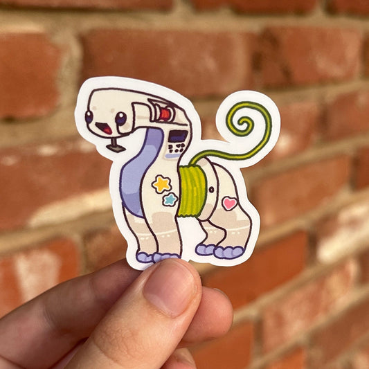 A hand holding a die-cut sticker of a personified sewing machine, set against a blurred red brick wall background.